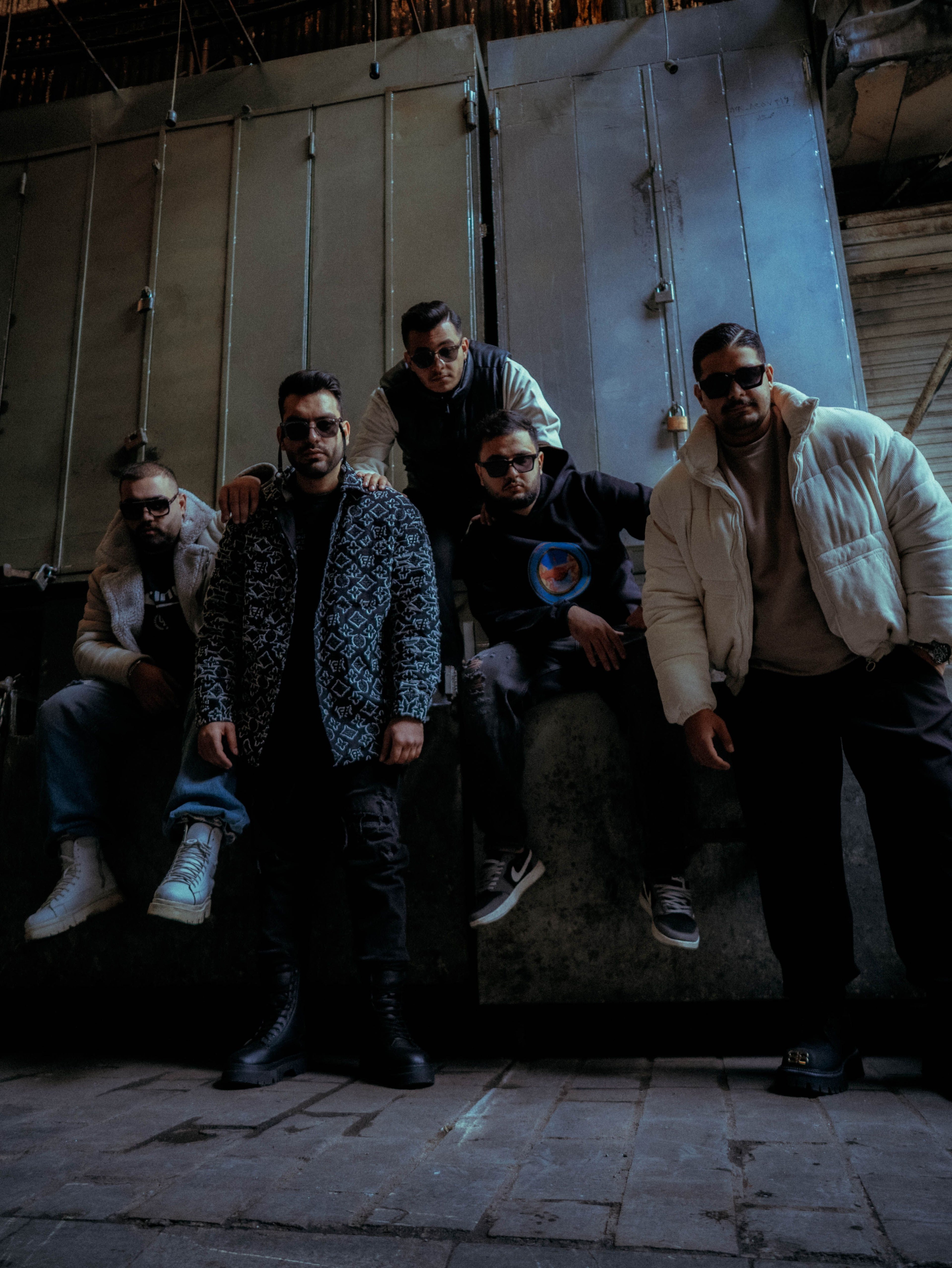 Group of men in urban streetwear posing against dark industrial backdrop