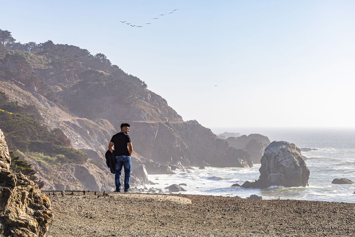 Man in fitted black tee with denim jeans outdoors — lifestyle shot showing medium build